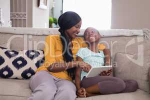 Mother and daughter using digital tablet while sitting on sofa at home