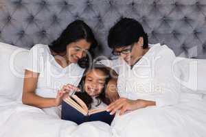 Smiling multi-generation family reading book while resting on bed