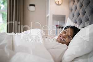 Smiling mature woman resting on bed at home
