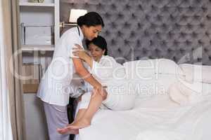 Nurse helping patient on bed at home