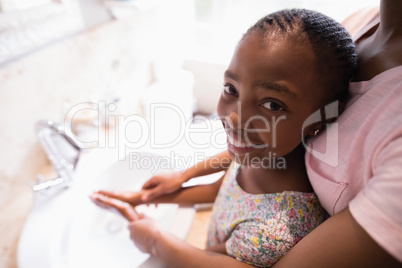 Mid section of mother assisting daughter while washing hands