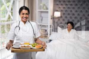Nurse holding breakfast tray while patient lying on bed at home