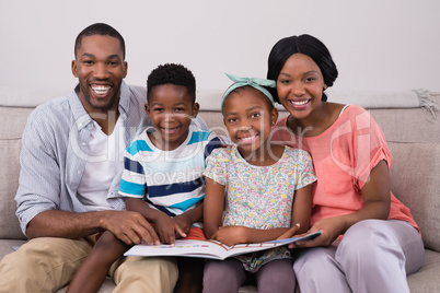 Smiling family holding magazine while sitting on sofa at home