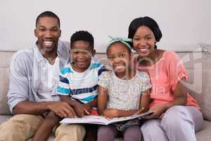 Smiling family holding magazine while sitting on sofa at home