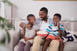 Cheerful father and children with popcorn sitting on sofa