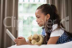 Side view of smiling girl using digital tablet while lying on bed