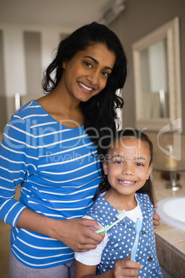 Smiling girl with mother holding toothbrushes in bathroom