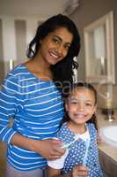 Smiling girl with mother holding toothbrushes in bathroom