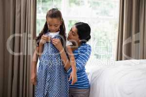 Mother helping daughter to dress up in bedroom