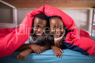 Portrait of smiling siblings lying under blanket