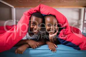 Portrait of smiling siblings lying under blanket