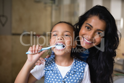 Girl brushing teeth with mother in bathroom