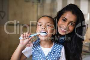 Girl brushing teeth with mother in bathroom