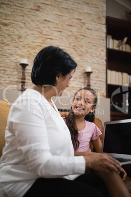 Smiling girl with grandmother holding laptop at home