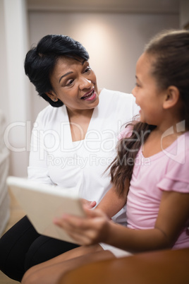 Woman sitting with granddaughter using digital tablet