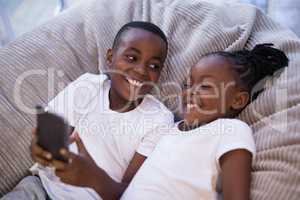 Smiling siblings using mobile phone while lying on couch