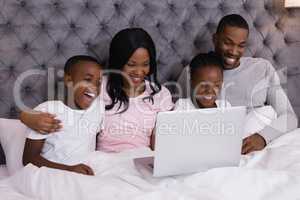 Happy family using laptop while sitting together on bed