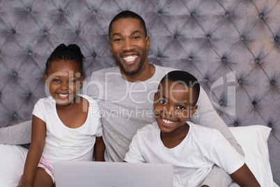 Portrait of happy father with children sitting on bed