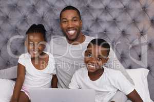 Portrait of happy father with children sitting on bed