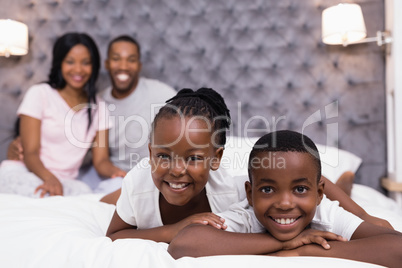 Portrait of siblings lying on bed with parents sitting in background