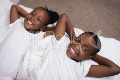 Portrait of smiling siblings lying together on bed