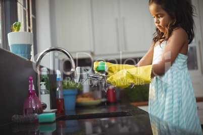 Cute little girl washing utensil in kitchen sink