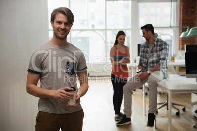 Portrait of executive holding coffee cup while colleague discussing in background