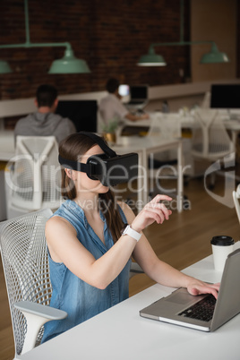 Female executive using virtual reality headset while using laptop