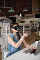 Female executive using virtual reality headset while using laptop