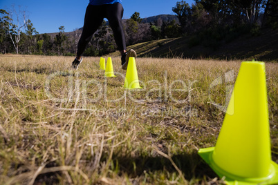 Low-section of woman running through training cones