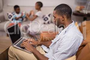 Young man using laptop while children playing at home