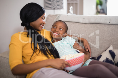 Mother and daughter having popcorn while resting on sofa at home