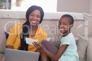 Happy mother and daughter holding laptop and mobile phone at home