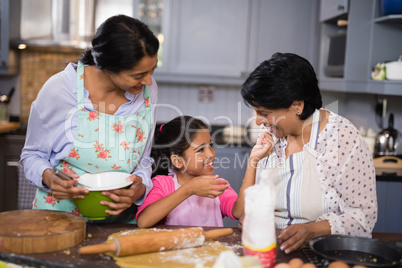 Smiling girl with mother and grandmother preparing food in kitchen