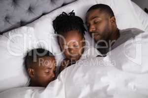 Father with children sleeping together on bed at home