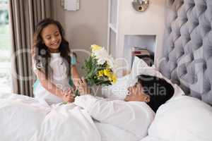 Smiling girl giving bouquet to sick grandmother at home