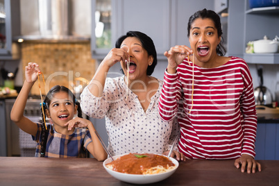 Happy multi-generation family eating spaghetti in kitchen