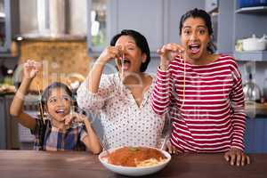 Happy multi-generation family eating spaghetti in kitchen