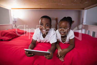 Happy siblings with digital tablet lying on bed at home