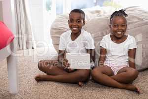 Portrait of happy siblings with digital tablet sitting on rug