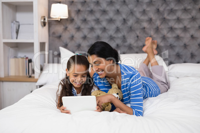 Mother and daughter using digital tablet while lying on bed at home