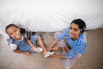 Portrait of mother helping daughter to wear shoe at home