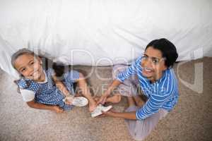 Portrait of mother helping daughter to wear shoe at home