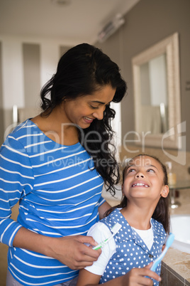 Girl with mother holding toothbrushes in bathroom