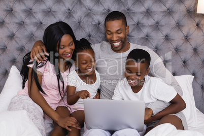 Happy family using laptop together on bed