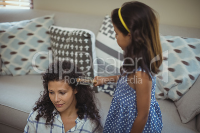 Cute daughter combing mothers hair in living room