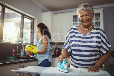 Mother ironing clothes while daughter washing utensil