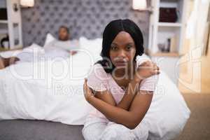 Young woman sitting while man lying on bed at home