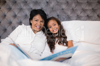 Portrait of happy grandmother and granddaughter reading book on bed