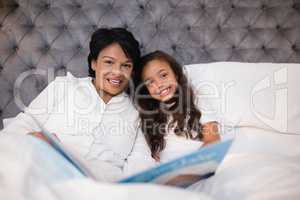 Portrait of happy grandmother and granddaughter reading book on bed
